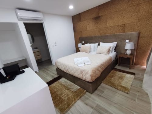 Quarto moderno na Villa Alzira em Seia com cama estofada em castanho, parede de cortiça, pavimento em madeira, luminárias brancas e casa de banho privativa