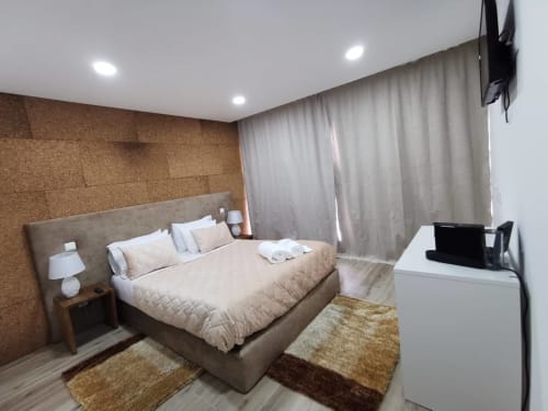 Quarto moderno na Villa Alzira em Seia com cama queen, parede de cortiça, TV e vista para o jardim através de cortinas translúcidas