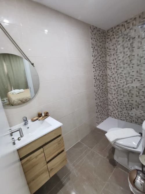 Casa de banho moderna da Villa Alzira com penteadeira em madeira, lavatório branco, sanita, parede de azulejo texturizado e espelho redondo em Seia