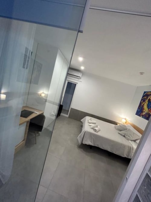Suite Deluxe del Hostal Fornet Altea con cama de sábanas blancas, divisor de vidrio, escritorio y comodidades modernas