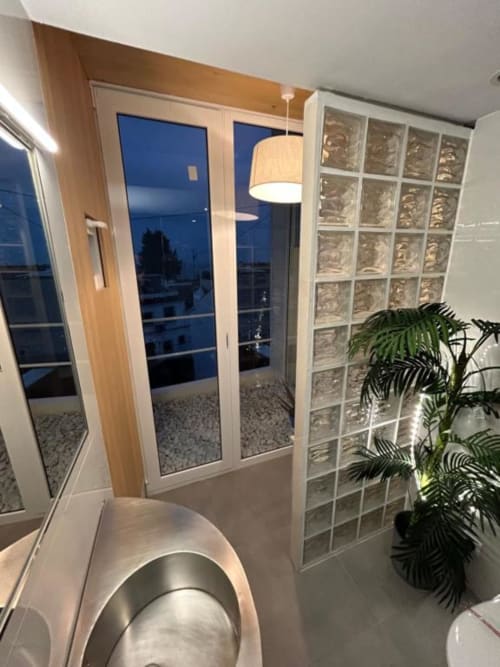 Baño moderno del Hostal Fornet Altea con pared de ladrillo de vidrio, equipamiento contemporáneo y puertas con vistas al mar que se abren al balcón