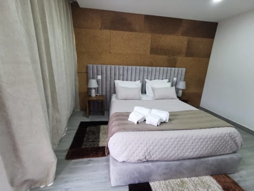 Quarto moderno da Villa Alzira com cabeceira estofada cinzenta, roupa de cama branca, parede de cortiça e vista para a montanha em Seia