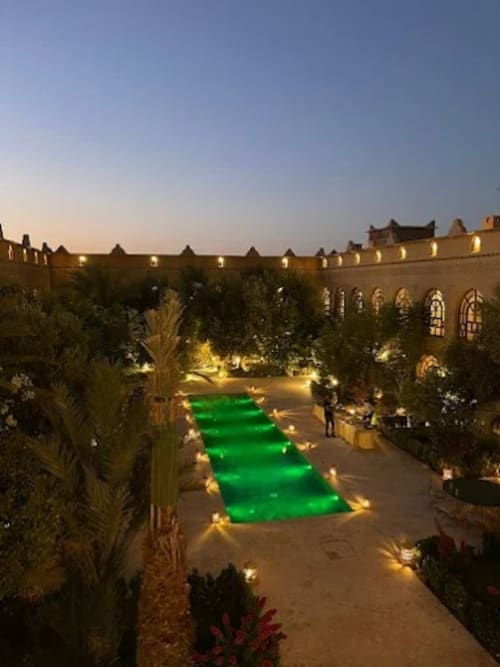 Cour de l'hôtel Eucalyptus au crépuscule avec piscine verte illuminée, palmiers et architecture traditionnelle à El