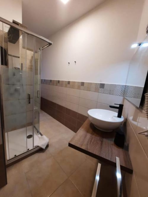 Bagno moderno della U Baruni b&b di Messina con box doccia in vetro, lavabo bianco a semisospensione e finiture in piastrelle marroni