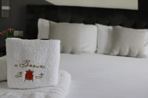 Asciugamano bianco arrotolato con logo ricamato sul letto della Family Room di U Baruni b&b a Messina, con cuscini e vista sulla città