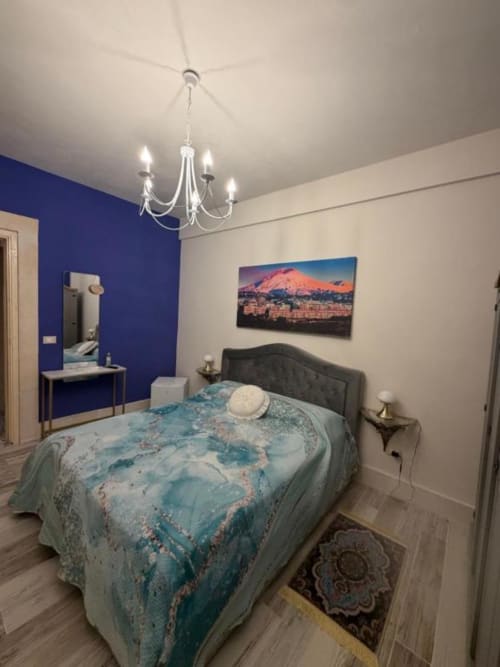 Camera da letto moderna a Villa Brikinnia con parete azzurra, letto matrimoniale, quadri montani, lampadario e toletta a Lentini