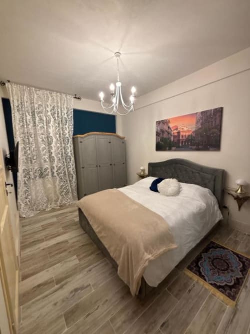Camera moderna a Villa Brikinnia a Lentini con letto matrimoniale, testata grigia, lampadario, armadio e tende a motivi