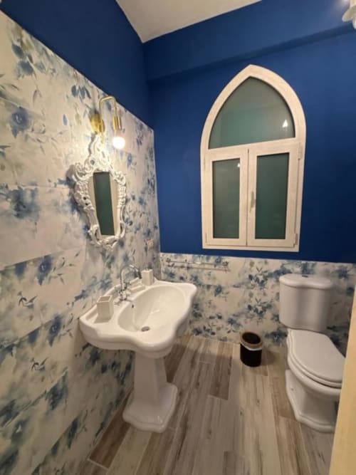 Bagno moderno di Villa Brikinnia con pareti blu, carta da parati floreale, lavabo con piedistallo, toilette e finestra ad arco a Lentini