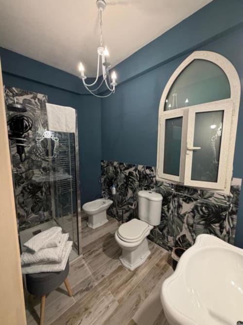 Bagno moderno di Villa Brikinnia con pareti turchesi, dettagli piastrelle decorate, sanitari bianchi, specchio ad arco, doccia walk-in