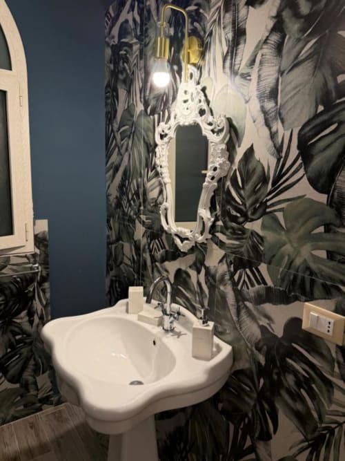 Bagno moderno con specchio bianco ornamentale, lavabo su colonna bianca e carta da parati botanica nera a Villa Brikinnia B&B