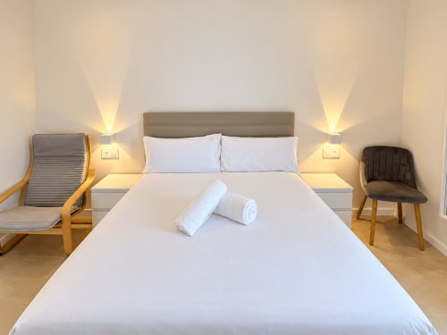 Dormitorio moderno en apartamento Holibai de Baiona con cama doble, sábanas blancas e iluminación ambiental de lámparas de mesita