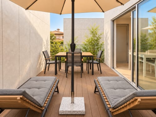Terraza moderna del apartamento Holibai en Baiona con tumbonas, mesa de comedor, sombrilla y vistas a la ciudad