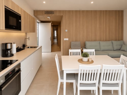 Cocina y sala de estar de apartamento moderno de 2 habitaciones en Baiona con detalles de madera, sillas blancas y sofá gris
