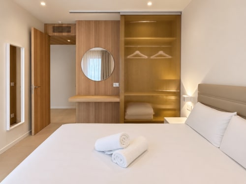 Dormitorio moderno en apartamento Holibai de Baiona con armario de madera, espejo redondo y ropa de cama blanca
