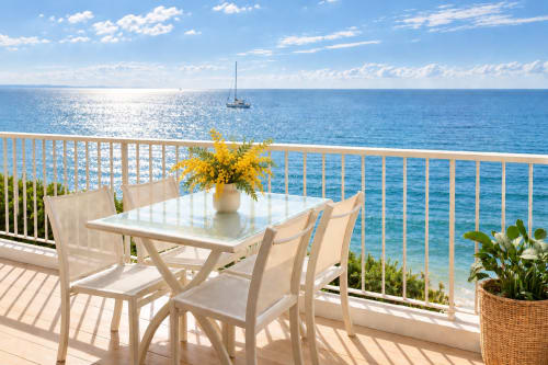 Balcon vue mer à Cannes avec table à manger, fleurs jaunes et voilier en Méditerranée