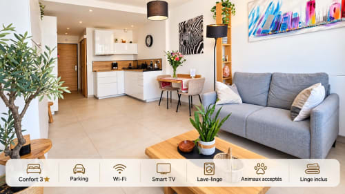 Le Nid du 9 studio à Aix-les-Bains : salon lumineux avec canapé gris, kitchenette, table à manger, plantes et vue sur la ville