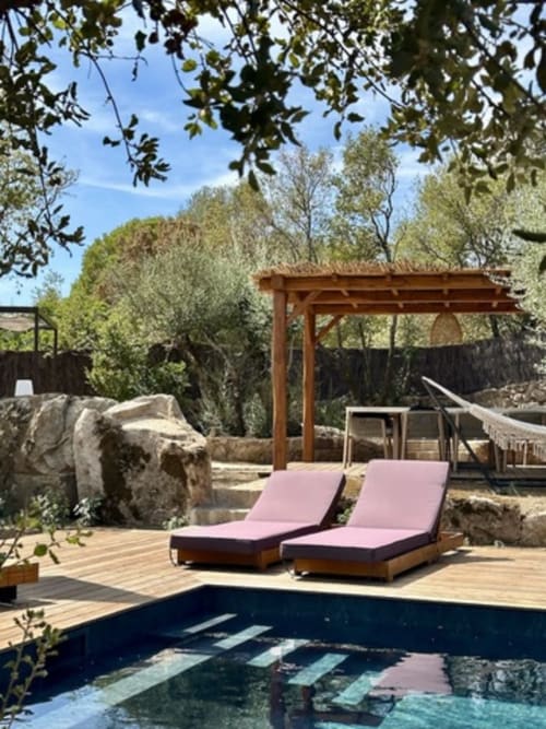 Espace de détente au bord de la piscine des Villas d'A Storia à Porto-Vecchio avec chaises longues roses, terrasse en bois, pergola et arbres environnants