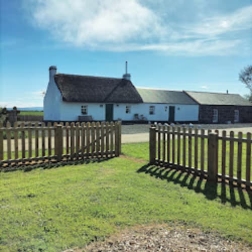 Ballymultimber Cottages, Cissy's Cottage in Limavady with white-washed walls, thatched roof, wooden fence, and mountain views