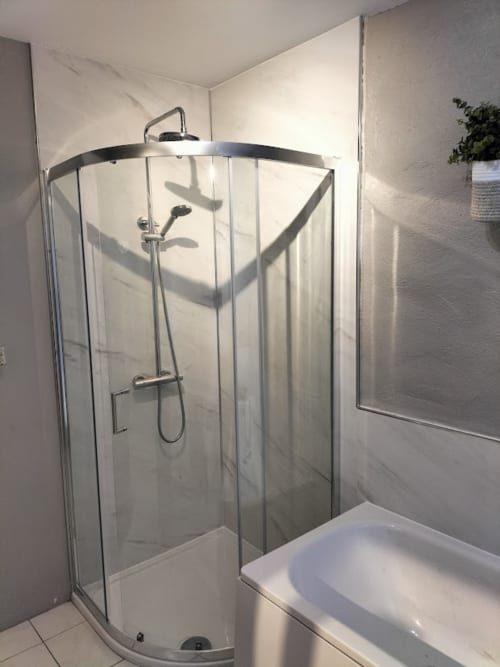 Modern curved glass shower enclosure with chrome fixtures and rainfall showerhead in The Barn cottage at Ballymultimber,
