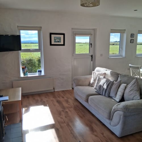 Bright living room at Ballymultimber Cottages with grey sofa, TV, and scenic views of green fields in Limavady