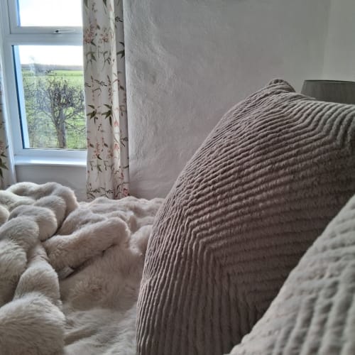 Cozy bedroom at Ballymultimber Cottages with textured pillows, white blankets, and countryside view through window in