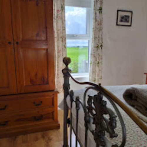 Bedroom with wrought iron bed frame overlooking green mountain landscape through window at Ballymultimber Cottages, Limavady
