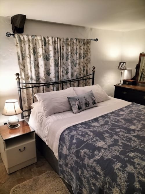 Cozy bedroom at Cissy's Cottage in Limavady with wrought iron bed, floral curtains, white bedding, and bedside lamp