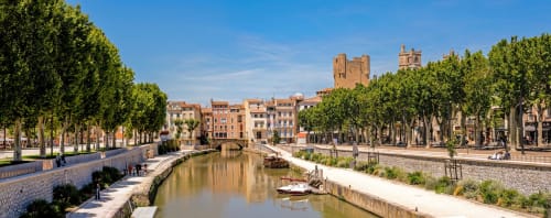 Tree-lined canal with historic buildings and church tower in Fontcouverte, France