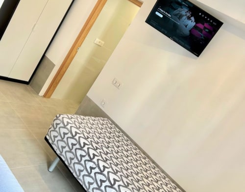 Habitación moderna del Hostal Fornet Altea con cama estampada, TV mural, detalles de madera y paredes blancas en Altea, España