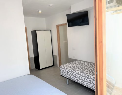 Habitación moderna en Hostal Fornet Altea con dos camas, armario, TV de pared y puerta con marco de madera en Altea, España.