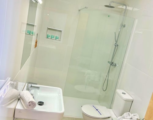 Baño moderno del Hostal Fornet Altea con mampara de ducha de cristal, lavabo blanco, inodoro y toallas blancas