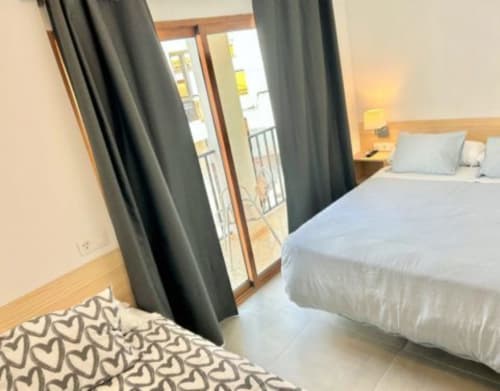 Dormitorio moderno en Hostal Fornet Altea con camas gemelas, cortinas grises y puertas al balcón con vistas a la costa