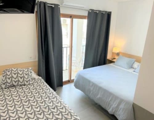 Moderna habitación doble en Hostal Fornet Altea con camas azules, acceso a balcón y cortinas oscuras en Altea, España