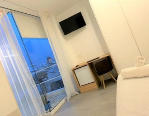 Habitación moderna de Hostal Fornet Altea con TV mural, escritorio de madera, vista de balcón y decoración minimalista