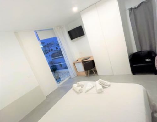 Habitación moderna en Hostal Fornet Altea con cama blanca, escritorio, TV y balcón con vistas azules al atardecer
