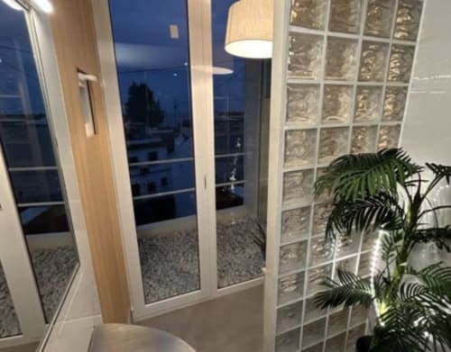 Moderna habitación de hotel con puertas de cristal, pared de bloques decorativos, planta en maceta y vistas de la ciudad al atardecer en Hostal Fornet Altea