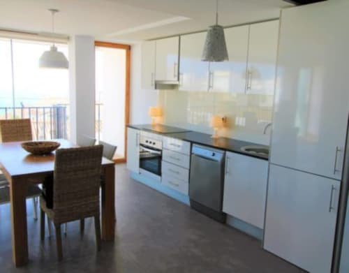 Cocina y comedor modernos en Hostal Fornet Altea con muebles blancos, encimera negra y balcón con vistas al mar