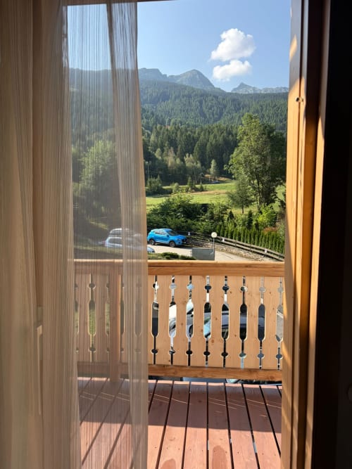 Vista montagnosa dal balcone di Villa Brioschi ad Aprica con ringhiera in legno e auto blu parcheggiata sottostante