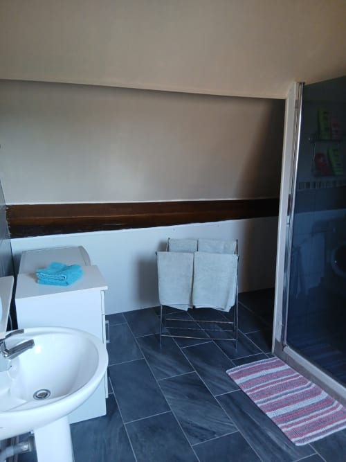 Salle de bains moderne avec lavabo blanc, carrelage sombre, porte-serviettes et étagère de rangement au gîte Chez Robins à Trie-Château