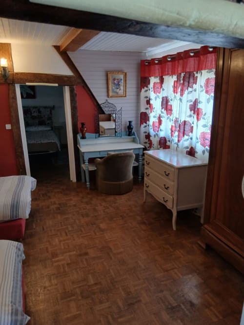 Chambre de cottage Chez Robins avec accents rouges, coiffeuse blanche, rideaux fleuris, poutres apparentes, Trie-Château