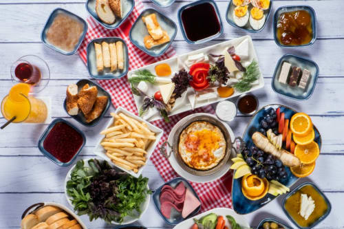 Petit-déjeuner du Yasi Hostel Lyon : charcuterie, viennoiseries, fruits, fromage, sauces, boissons, œufs et légumes frais sur fond blanc