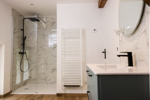 Salle de bain moderne du gîte Les Cabanes du Nideck avec douche en marbre, sèche-serviettes blanc, robinetterie noire et miroir rond