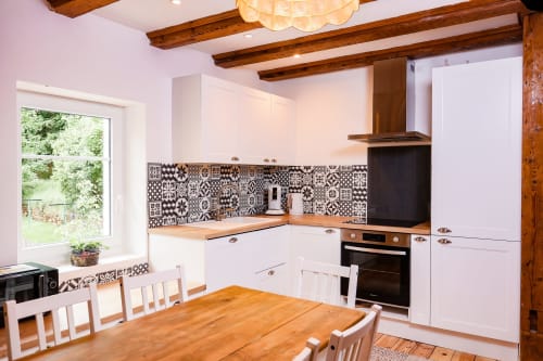 Cuisine moderne du gîte La Maison du Gardien avec armoires blanches, dosseret carrelage noir et blanc à motifs, poutres en bois