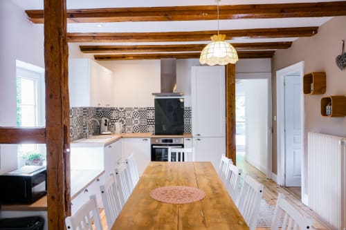 Cuisine chaleureuse avec poutres en bois, placards blancs, dosseret motifs et table en bois aux Cabanes du