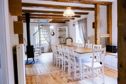 Spacieuse salle à manger du gîte La Maison du Gardien à Oberhaslach avec poutres en bois, chaises blanches et vue sur les montagnes