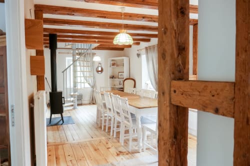 Salle à manger rustique aux poutres apparentes, chaises blanches et aménagement ouvert aux Cabanes du Nideck
