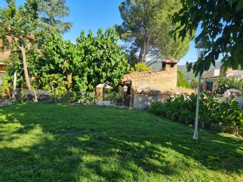 Exuberante jardín con césped verde, árboles y casa de piedra en Las Casitas de Noe, retiro rural en Madrid, España