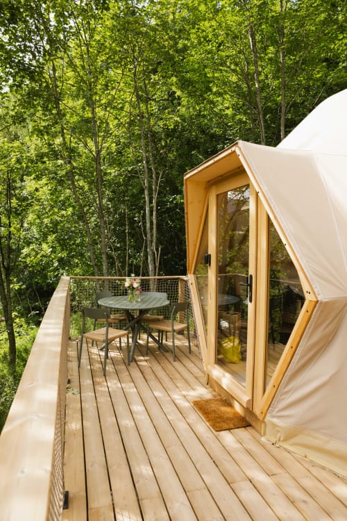 Cabane géodésique contemporaine avec terrasse en bois, portes vitrées et espace repas extérieur entouré d'une forêt luxuriante aux Cabanes du