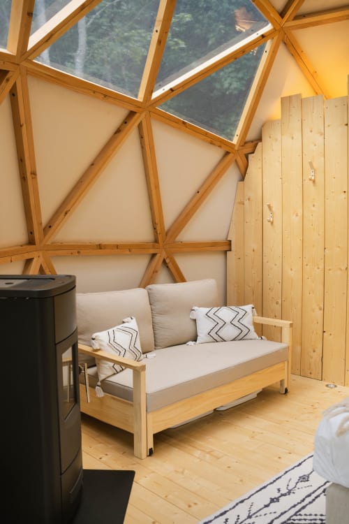 Intérieur douillet de dôme géodésique en bois avec canapé crème, vue panoramique sur la forêt d'Oberhaslach, et poêle en bois noir aux Cabanes