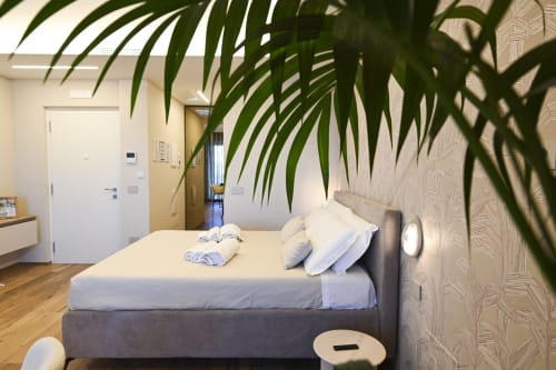 Modern bedroom at Vimini Apulian Experience with gray bed, white linens, potted plant, and minimalist décor in Bari